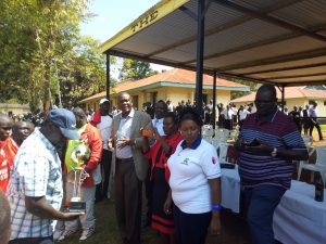 Nyanza Region's Sports Chair, Mr. Moses Adala in checked coat, addressing Regional Championship participants at a past event. With him is the Regional Secretary, Mr. Tom Thomas Odhiambo; holding a trophy.