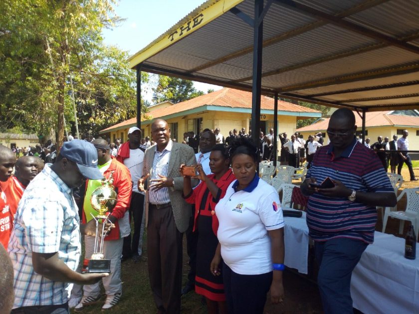 Nyanza Region's Sports Chair, Mr. Moses Adala in checked coat, addressing Regional Championship participants at a past event. With him is the Regional Secretary, Mr. Tom Thomas Odhiambo; holding a trophy.